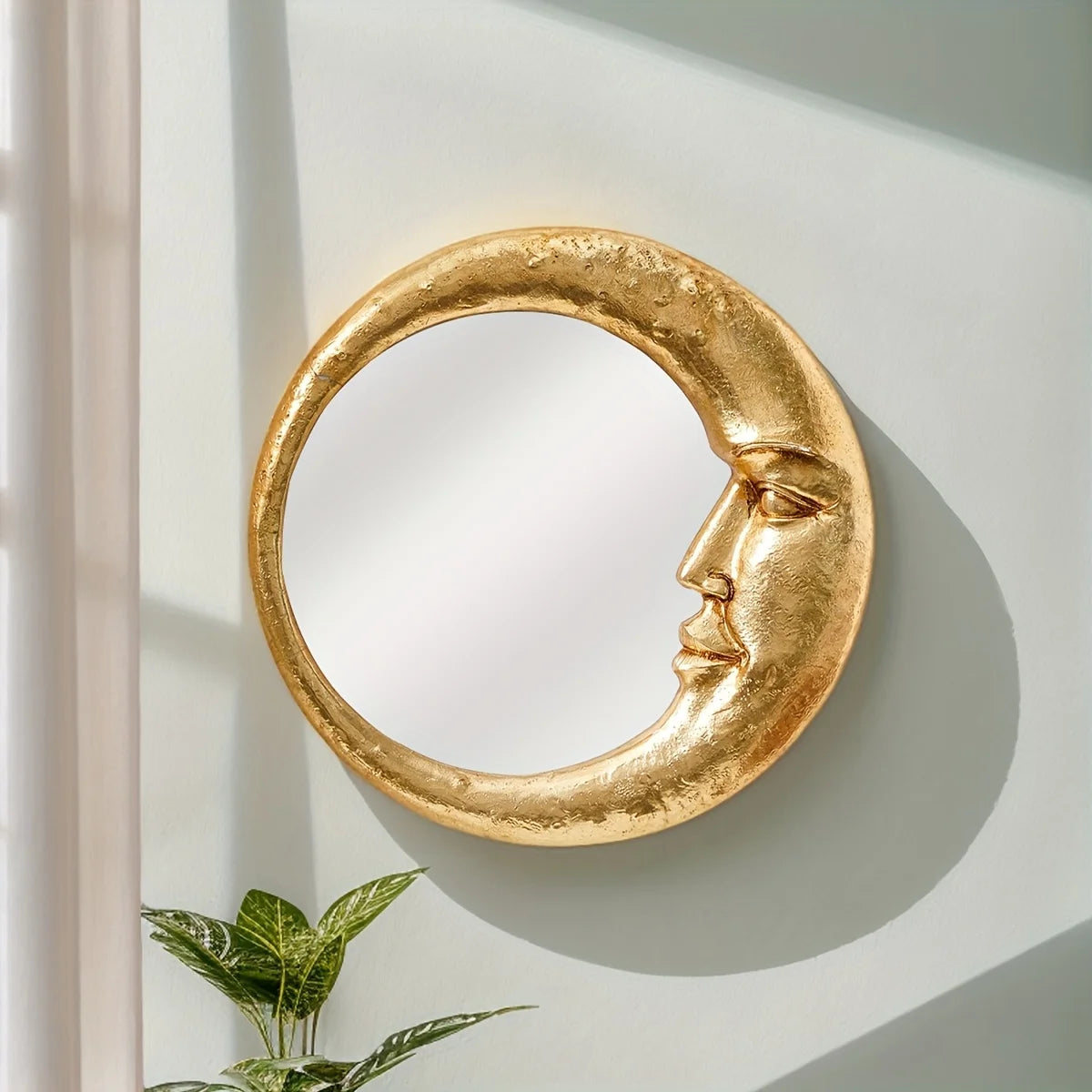 A round, gold resin decorative hanging mirror shaped like a crescent moon is mounted on a light-colored wall.