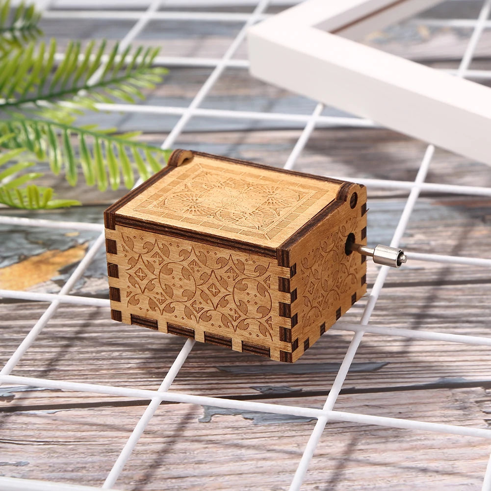 A vintage hand crank music box made of light brown wood with intricate carvings resting on a white grid surface.
