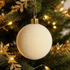 A white velvet flocked Christmas ornament hanging on a green pine branch with gold tinsel.