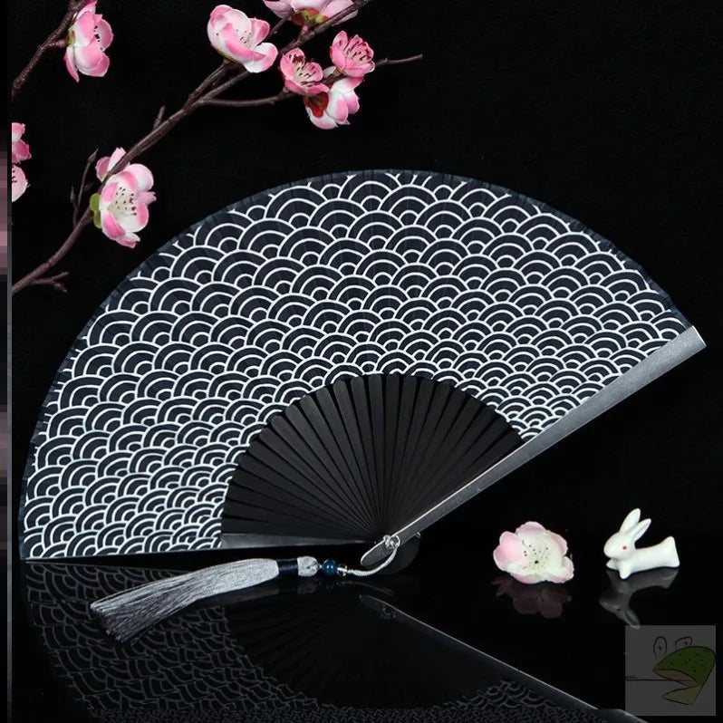 A black and white fan with a traditional Japanese pattern is shown against a dark background.