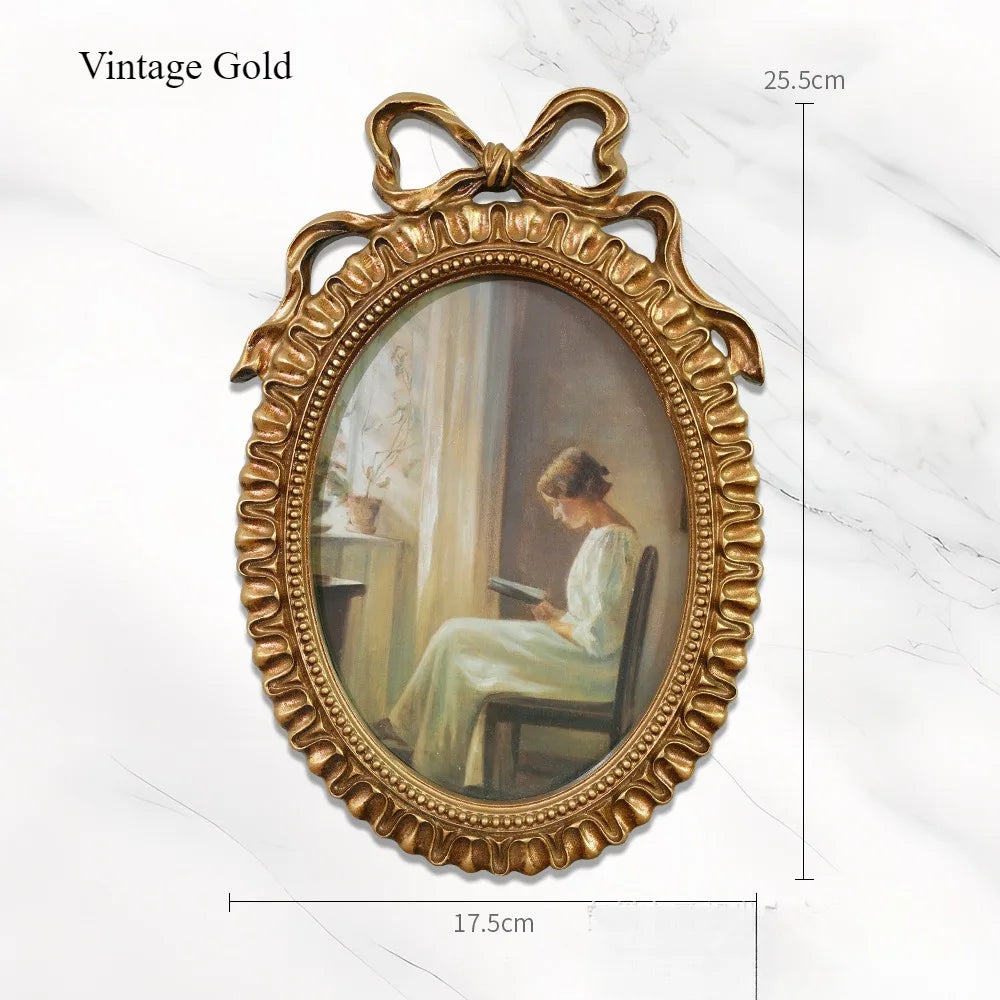 A vintage gold bowknot picture frame with an oval painting of a woman seated.