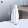 A white ceramic bud vase with an elongated, curved shape is shown on a white surface.