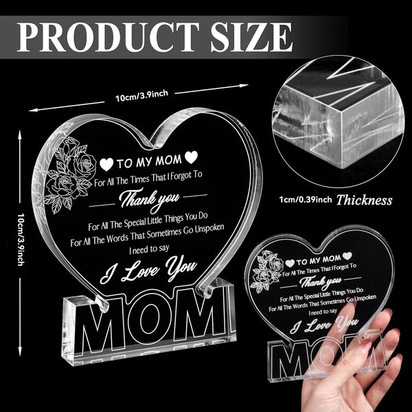 Plaque en acrylique cœur gravée 'I Love You Mom' et motifs floraux, à côté d'une main pour l'échelle.