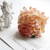 A bouquet of pink and cream silk hydrangea petals resting on a white surface next to a white angel figurine.