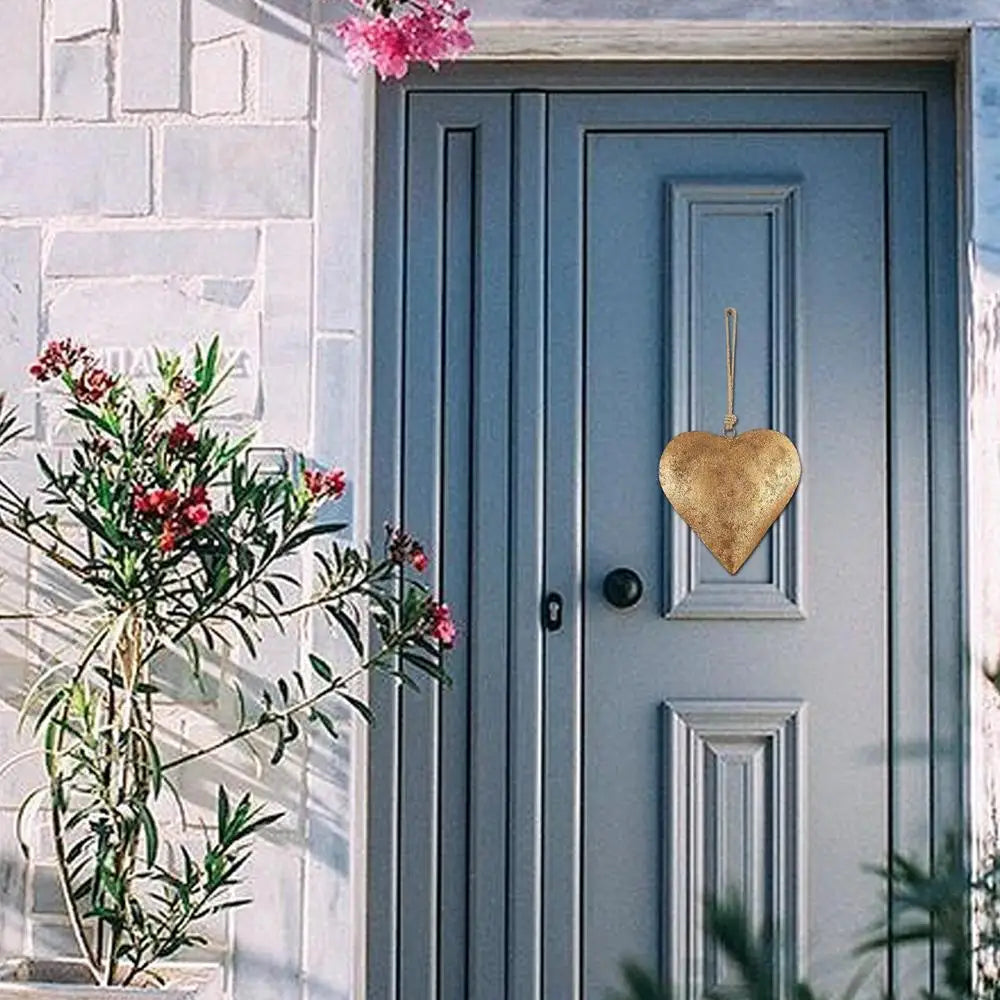A light blue wooden door with a gold heart decoration and greenery in the foreground.