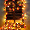 Warm orange maple leaf fairy string lights decorating a wooden window frame.