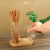 A hand pours incense sticks into a glass holder with a gold-colored metal rod and wooden base.