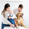 A mother holds a baby and a dog together on a table, demonstrating the use of an inkless pet paw print keepsake kit.
