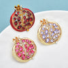 Gold-toned crystal pomegranate brooch pin featuring red and purple gemstones on a white background.
