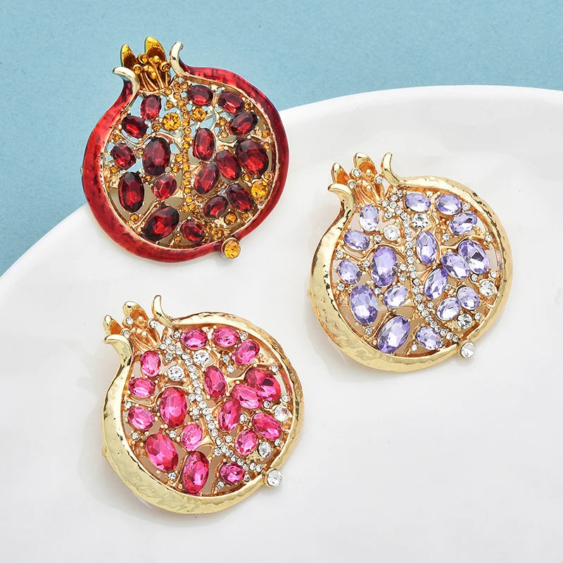 Gold-toned crystal pomegranate brooch pin featuring red and purple gemstones on a white background.