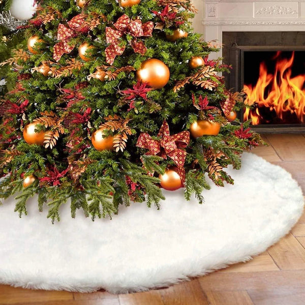 A lush green Christmas tree decorated with red and gold foliage sits on a white plush rug next to a fireplace.