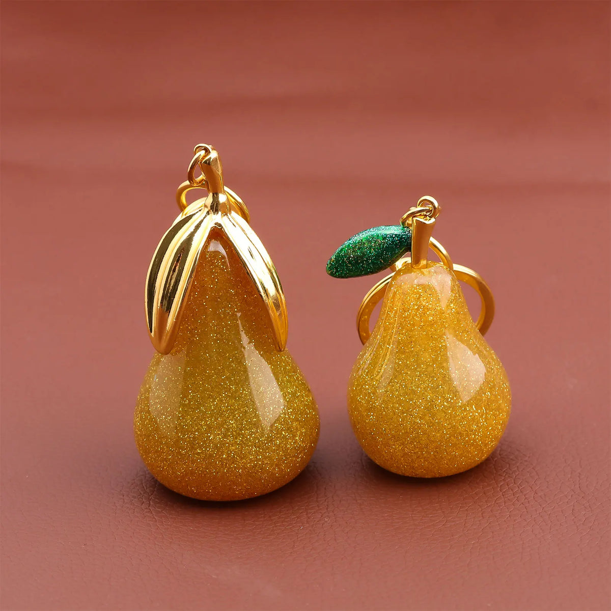 Gold-toned pear-shaped fruit keychain charm with a green gemstone detail.