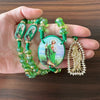 A hand holds a green crystal rosary necklace featuring Saint Jude and the Virgin Mary cross pendant.