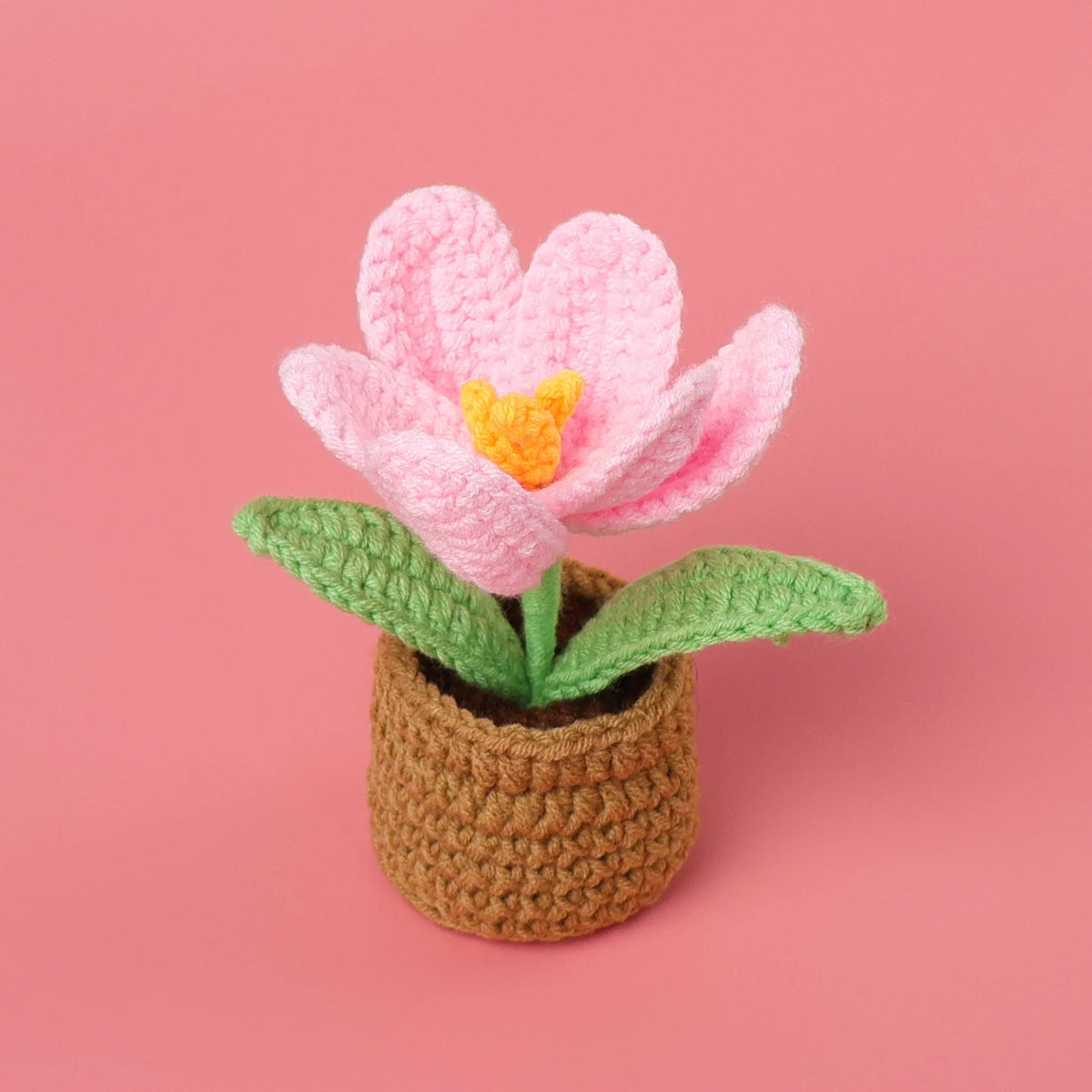 Handcrafted crochet pink tulip flower with a yellow center growing in a brown textured pot.