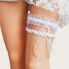 Ivory lace bowknot bridal garter set worn on a leg, visible under sheer white fabric.
