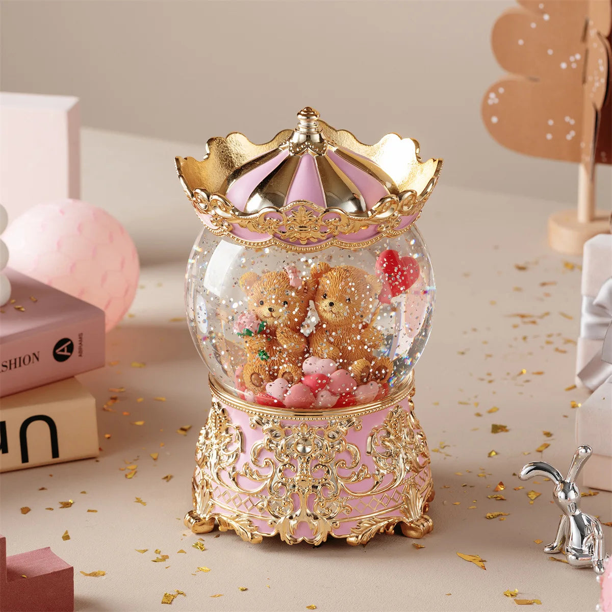 Adorno de caja de música con bola de cristal dorada y rosa lleno de osos de peluche sobre una superficie clara.