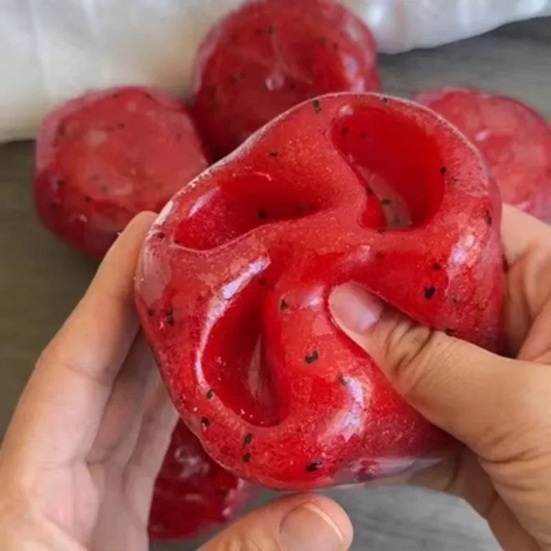 A hand holds a bright red watermelon slushy squishy fidget toy with visible black specks.