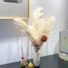 A dried pampas grass bouquet with reddish-brown plumes and small dried flowers in a white vase on a dark table.