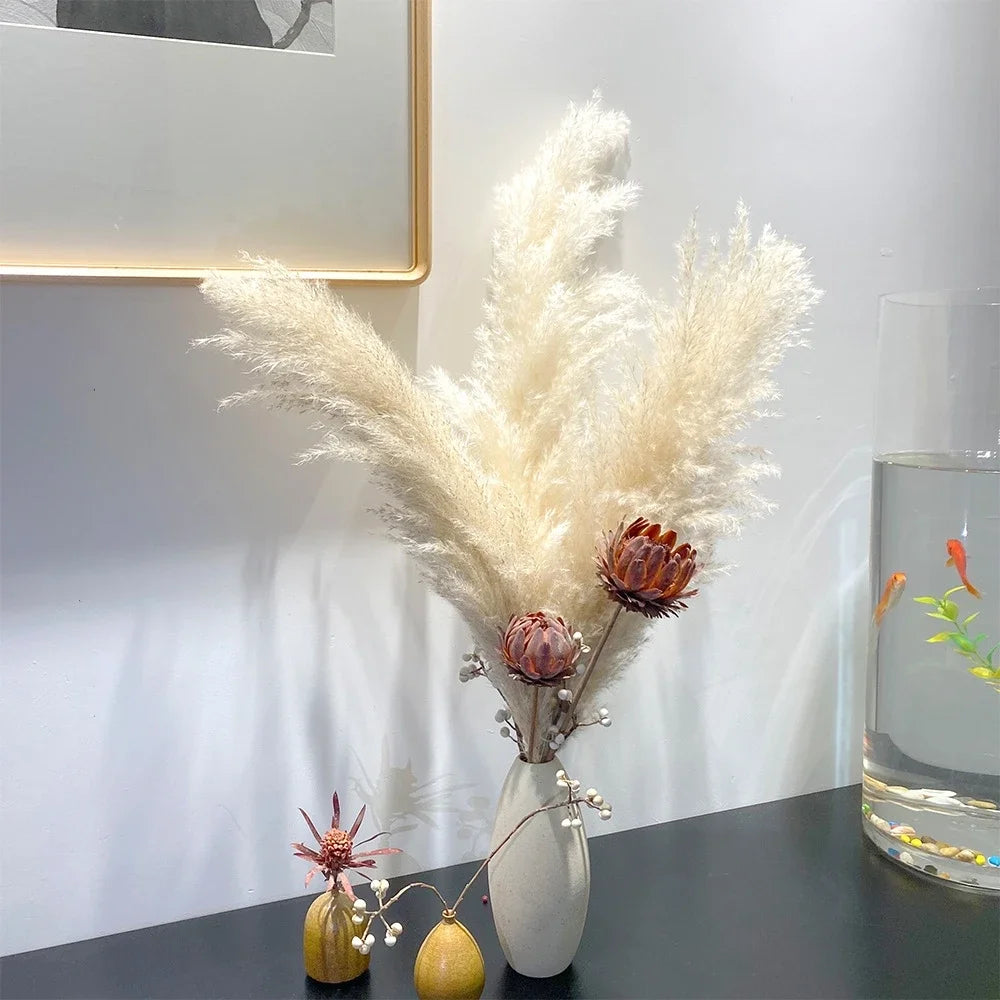 A dried pampas grass bouquet with reddish-brown plumes and small dried flowers in a white vase on a dark table.