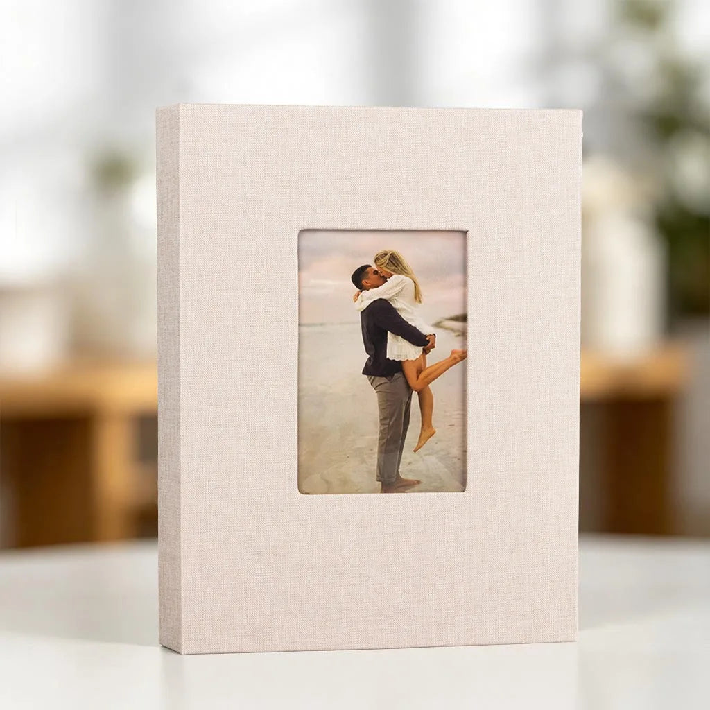 A square linen photo album with a front display window showing a couple embracing in a scenic outdoor setting.