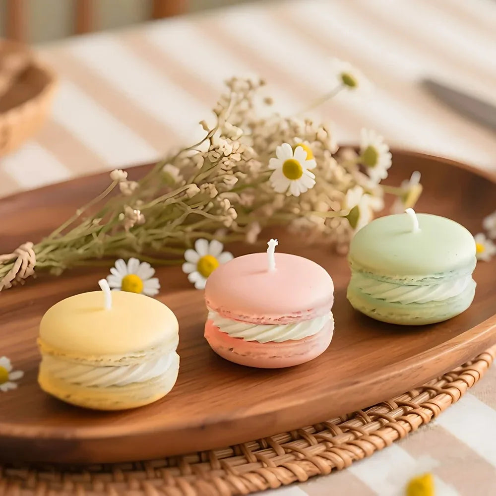A wooden platter displays several macaron-shaped soy wax candles in pastel pink and green colors with dried flowers.