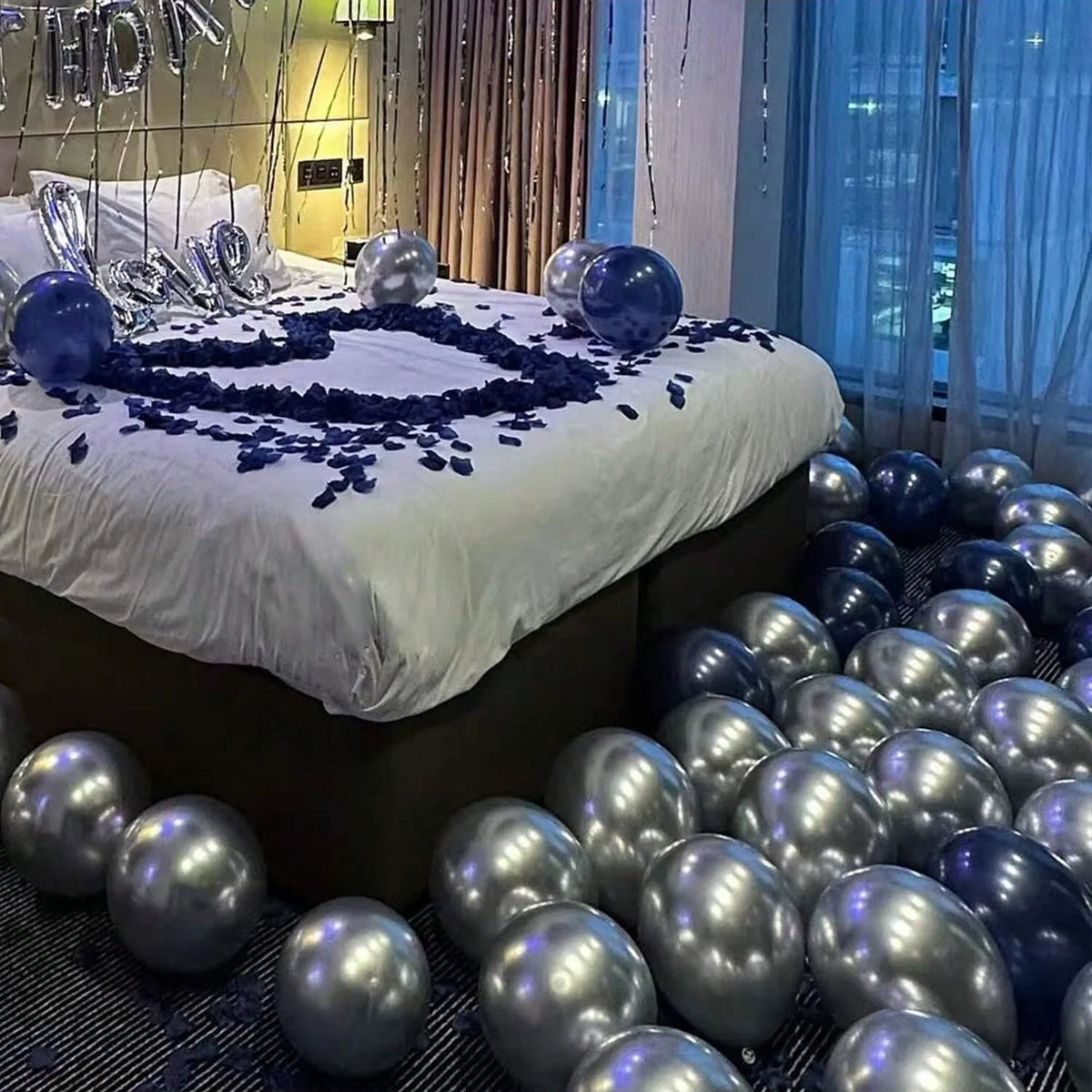 Eine Ansammlung von dunkelblauen und silbernen Ballons arrangiert auf einem Bett mit weißer Bettwäsche.