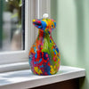 A colorful resin figurine of a frog with a white head, sitting on a windowsill.