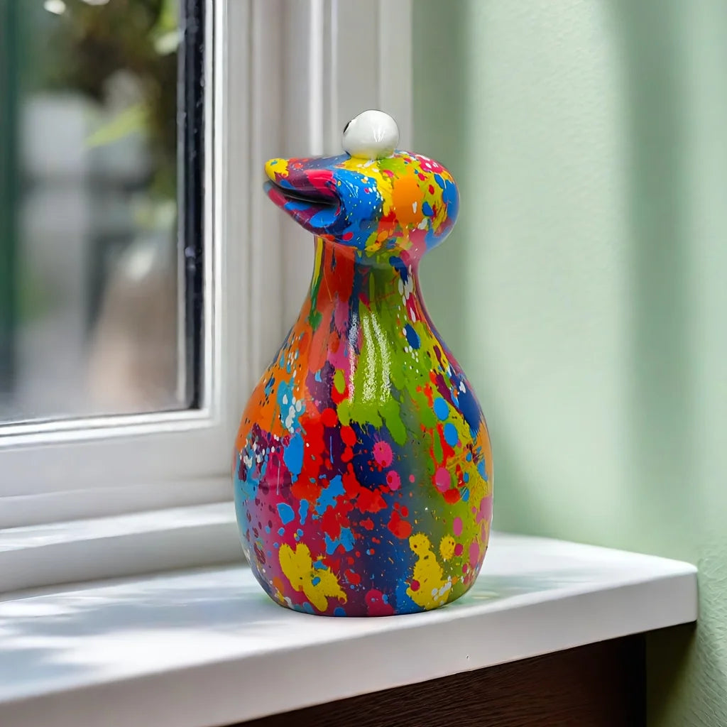 A colorful resin figurine of a frog with a white head, sitting on a windowsill.
