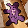 A purple cartoon monster rug with a pink eye and angry expression placed on a light wood floor.