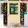 Vertikales Wandtuchbanner mit bunten Buchstaben 'BIENVENIDOS CLASES' hängt an einer hellgelben Tür.