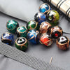 A collection of handcrafted lampwork glass beads with gold accents in various vibrant colors and textures arranged on a dark 