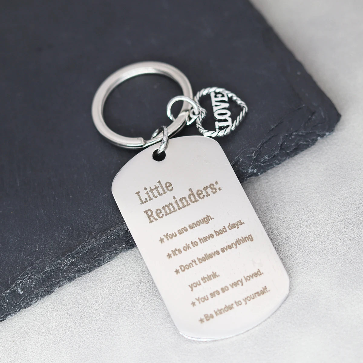 A silver stainless steel keychain with a heart charm engraved with five positive reminders.