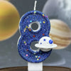A blue glitter number eight candle decorated with stars and a white planet design.