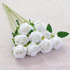 A bouquet of white velvet artificial roses with green stems arranged on a light fabric.