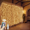 A hand holds a remote control device near a sheer curtain illuminated by warm fairy lights.