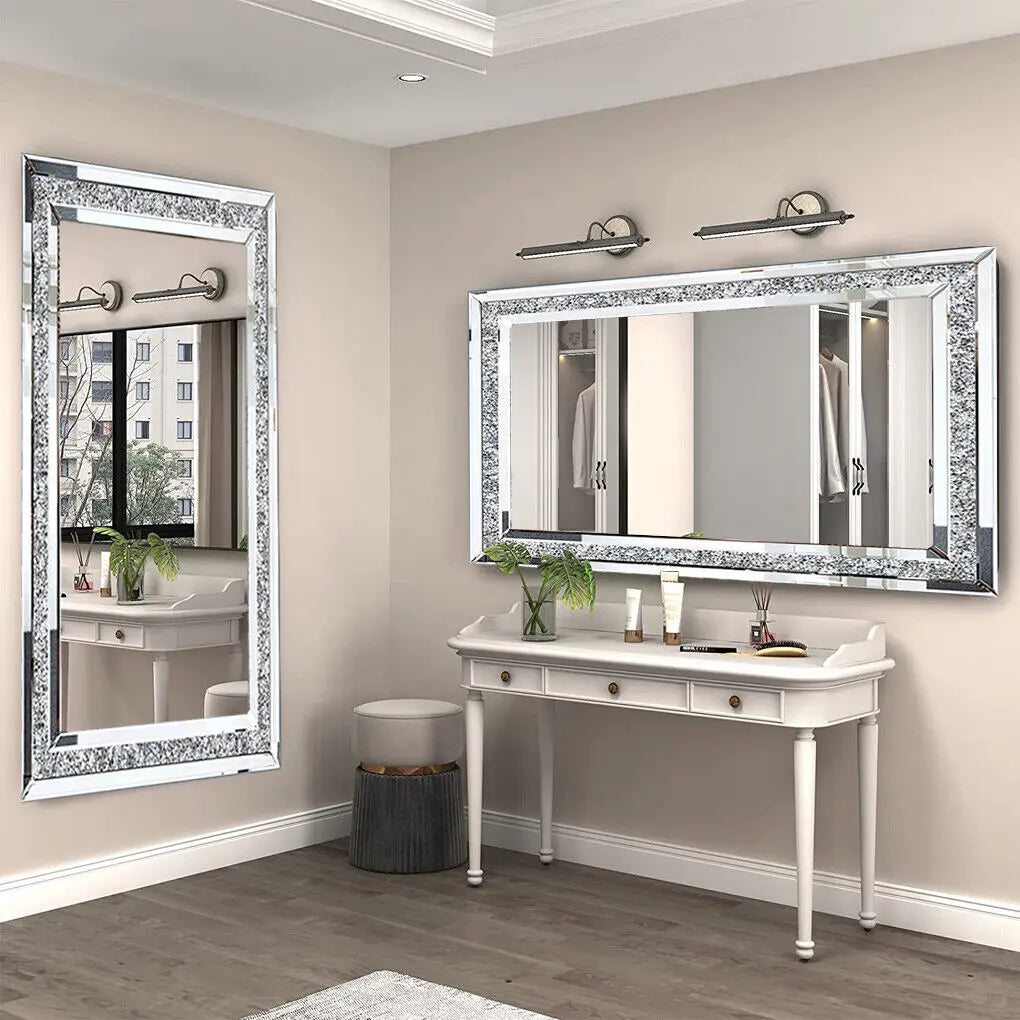 A rectangular silver crystal rhinestone wall mirror with a sparkling frame mounted above a white vanity table.