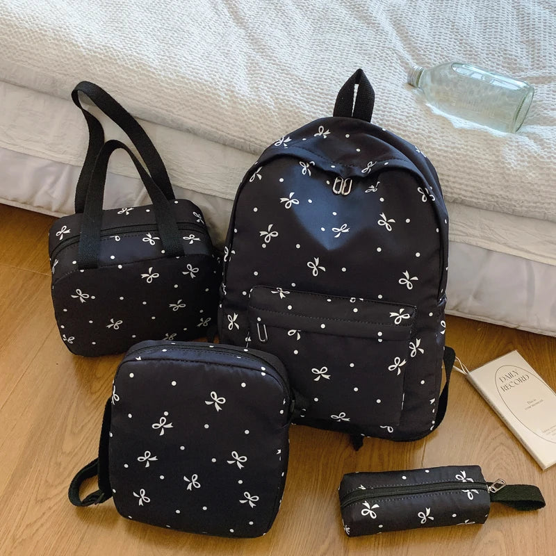 A black bow print backpack set includes a main backpack and a smaller pouch, resting on a light-colored surface.