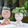 A pair of artistic resin girl faces, painted in soft earth tones, serve as planters for succulents.