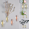 Modern wall-mounted flower vase featuring various dried branches and fresh flowers in gold and rose tones.