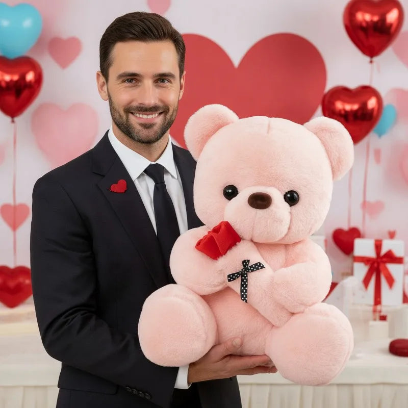 A man holds a pink rose bear plush toy with red ribbon and faux flowers against a pink heart background.