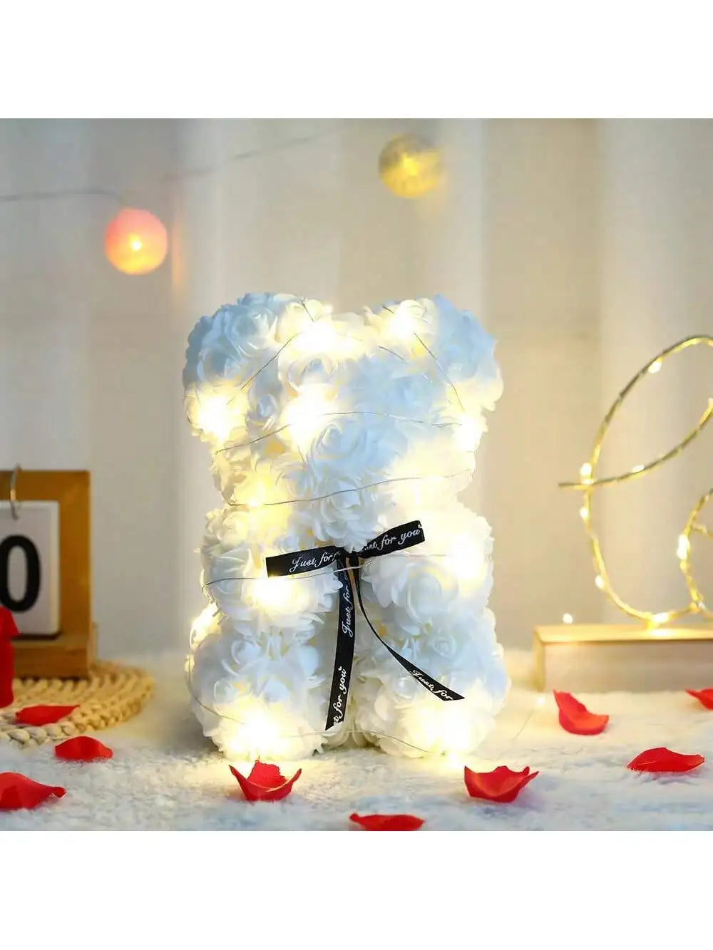 Weiße künstliche Rosen-Teddybär, beleuchtet mit warmem Licht auf einer weißen, flauschigen Oberfläche.