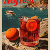 A glass of Negroni cocktail sits on a stone surface with an orange fruit nearby, set against a scenic background.