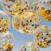 A close-up of clear balloons filled with gold confetti floating against a blue sky.