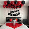 A bedroom decorated for a birthday, featuring a balloon garland above a bed with red and black balloons and a heart-shaped re