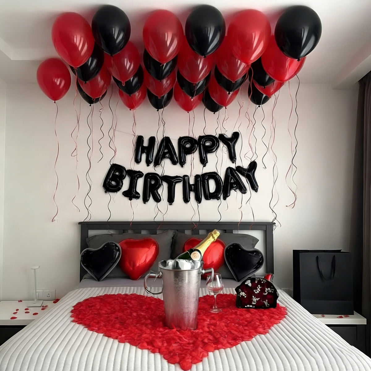 A bedroom decorated for a birthday, featuring a balloon garland above a bed with red and black balloons and a heart-shaped re