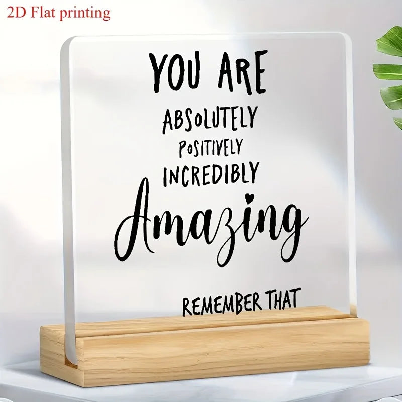 A clear acrylic desktop sign with black text that reads You are absolutely positively incredibly amazing