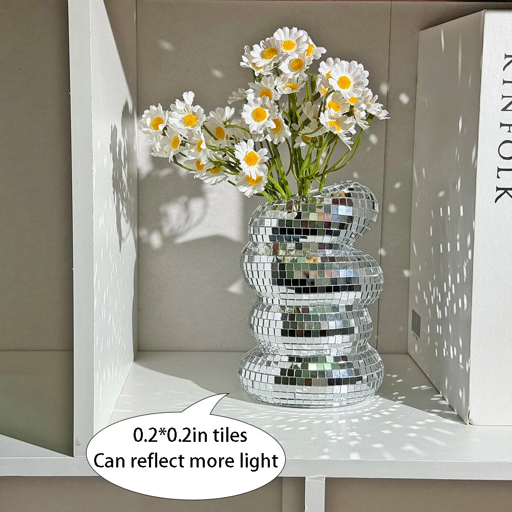 A glass vase filled with white daisies sits on a shelf, decorated with reflective mirror tiles.