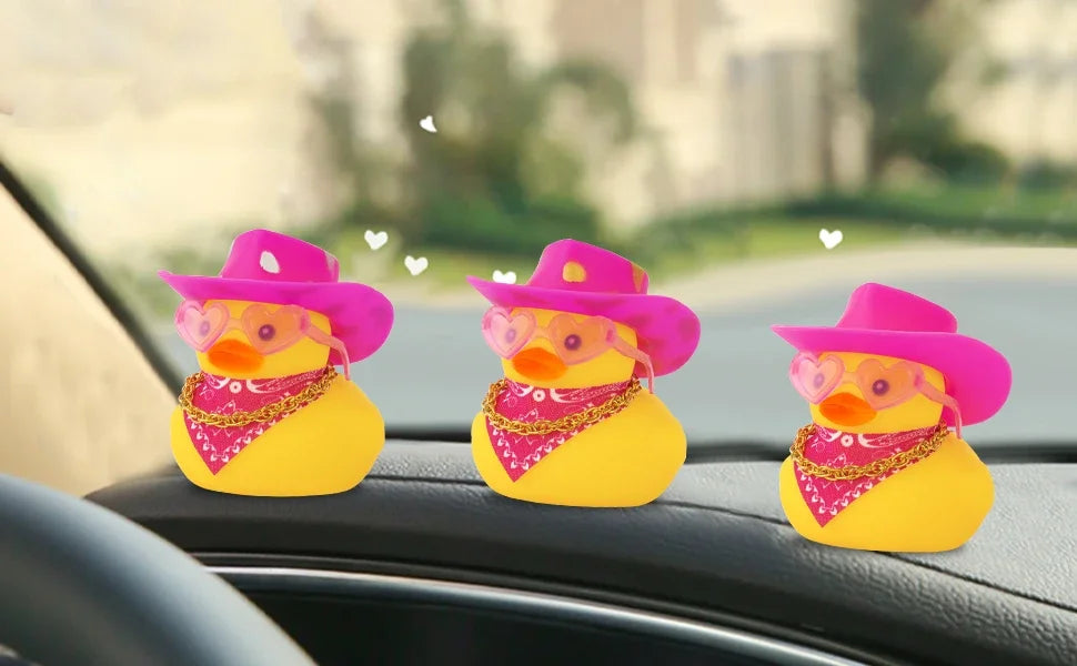 Three yellow rubber duck car dashboard decorations wearing pink cowboy hats on a black car interior.