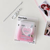 A pink heart-shaped photo album keychain with a clear cover and a silver chain is displayed on a white surface.