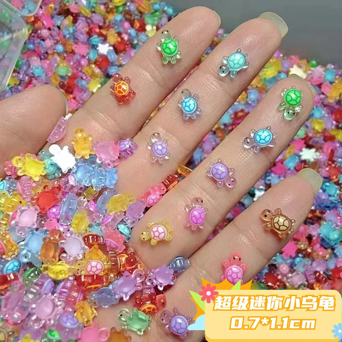 Una mano muestra 50 adornos de uñas miniatura de tortuga coloridos esparcidos sobre una superficie.